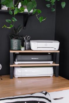 a printer sitting on top of a wooden shelf next to a potted green plant