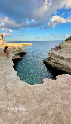 people are standing at the edge of a cliff by the water and looking out to sea