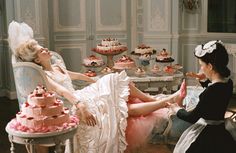 a woman sitting on a chair in front of a table filled with cakes