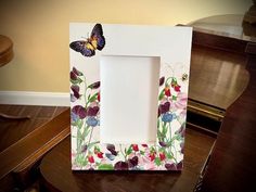 a white frame sitting on top of a wooden table next to a piano with a butterfly painted on it