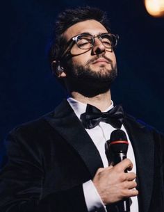 a man in a tuxedo holds a microphone and looks up at the sky