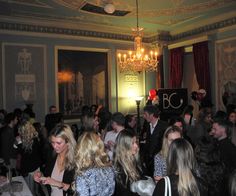 a large group of people standing in a room with chandelier and paintings on the walls