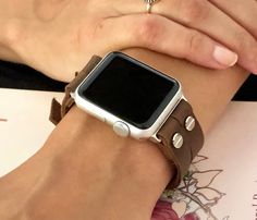 a woman wearing a brown leather bracelet with an apple watch on her wrist