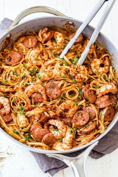 a skillet filled with shrimp and pasta on top of a white wooden table next to a napkin