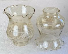 two clear glass vases sitting next to each other on a white tableclothed surface