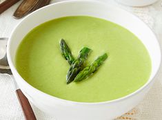 a white bowl filled with soup and asparagus on top of a table next to spoons