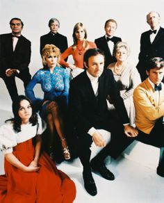 a group of people sitting next to each other in front of a white wall with one man wearing a suit