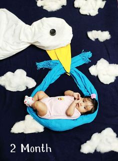 a baby is laying down on a cloud filled blanket with a large bird head hanging from it's side