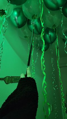 a person holding an umbrella in front of green balloons and streamers hanging from the ceiling