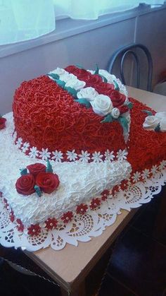 a large heart shaped cake on top of a table with white doily and red roses