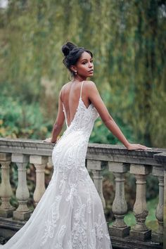 a woman in a wedding dress leaning on a railing looking off into the distance with her back to the camera