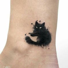 a black cat tattoo on the ankle with watercolor paint splatters all over it