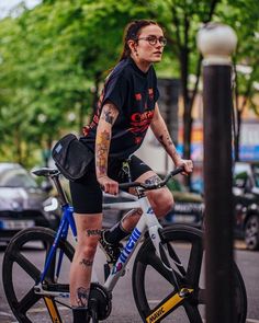 a woman with tattoos riding a bike down the street in front of a lamp post