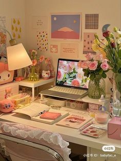 a laptop computer sitting on top of a desk next to a vase filled with flowers