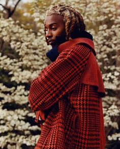 a man with dreadlocks is standing in front of some trees and white flowers