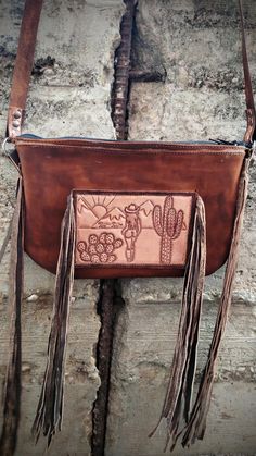 Tooled leather crossbody purse featuring a beautiful desert scene with a lonely cowgirl walking through. This purse has fringe on either side of the purse and on the front with the tooled leather piece.  Hand Tooled leather strap in a floral design. Western Style Hand Tooled Shoulder Bag For Travel, Western Style Crossbody Shoulder Bag For Travel, Bohemian Leather Bag With Concho, Beautiful Desert, Desert Scene, Hand Tooled Leather, Leather Crossbody Purse, Leather Pieces, Tooled Leather