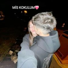 a man and woman hugging each other in front of a boat on the water at night