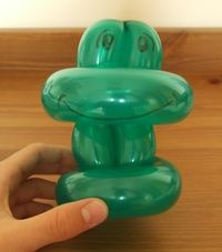 a green frog toy sitting on top of a wooden table next to a person's finger