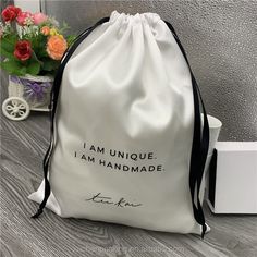 a white bag sitting on top of a wooden floor next to a vase with flowers