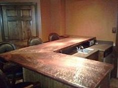 a kitchen counter with two sinks and chairs in front of the counter top is made out of wood