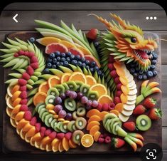 a wooden cutting board topped with fruit and dragon heads next to grapes, oranges, kiwis, strawberries