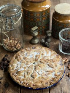 a pie sitting on top of a wooden table next to jars filled with nuts and other items