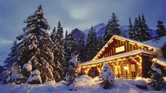 a cabin in the snow with christmas lights on it's roof and trees around