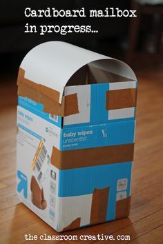 an open cardboard mailbox sitting on top of a wooden floor with the words, card board mail box in progress