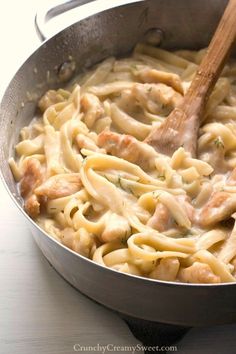 a pan filled with pasta and chicken on top of a stove next to a wooden spoon