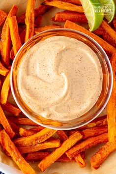 a white plate topped with sweet potato fries next to a bowl of ranch dressing and lime wedges