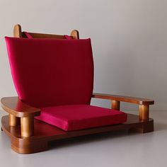 a red chair sitting on top of a wooden stand next to a white wall and floor