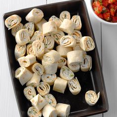 there are many rolls on the plate next to a bowl of salsa and a fork