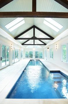 an indoor swimming pool in a house with white walls and ceiling beams, surrounded by windows