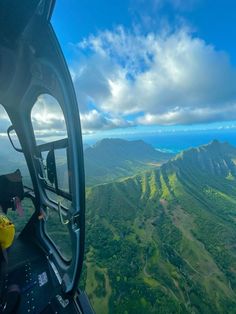 the view from inside an airplane looking down on green mountains and blue sky with clouds