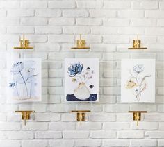 three paintings hanging on a brick wall in front of a white brick wall with gold brackets