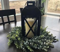 a lit candle on top of a wooden table next to a wreath with greenery