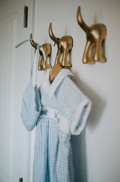 clothes hanging on hooks in front of a white door with gold deer head and coat hangers