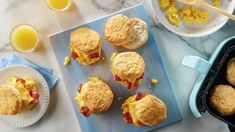 biscuits with eggs and bacon are on a blue cutting board next to some orange juice