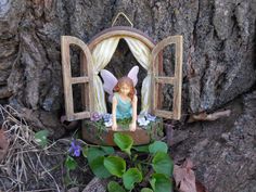 a fairy figurine sitting on top of a tree stump in front of a window