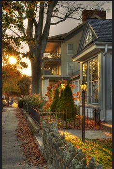 the sun is setting behind a house with many trees and bushes in front of it