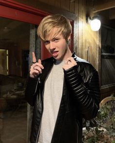 a young man in a black leather jacket pointing at the camera with his finger up