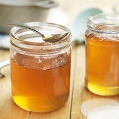 two jars filled with liquid sitting on top of a wooden table next to spoons