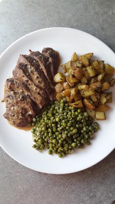 a white plate topped with meat, potatoes and peas