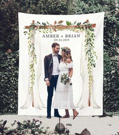 a newly married couple standing in front of an outdoor wedding ceremony sign with greenery