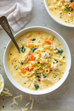 two bowls filled with chicken noodle soup on top of a white counter next to silverware