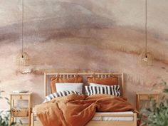 a bed with pillows and blankets on it in front of a wall painted with watercolors