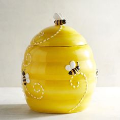 a yellow ceramic jar with bees painted on the side and white dots in the middle