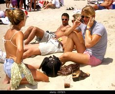 three people sitting on the beach talking on their cell phones and drinking beverages in front of them