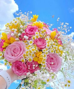 a bouquet of flowers is being held up by someone's hand in the sky