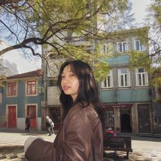 a woman standing in front of a tree on a city street with buildings behind her